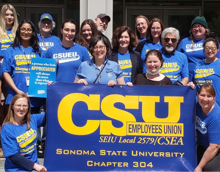Group of CSUEU Chapter 304 members dressed in blue and yellow and holding a union banner